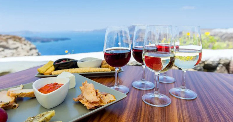 Horizontal color close-up image of greek appetizer. Tasting red, white and rose wine. Sea view in the background.